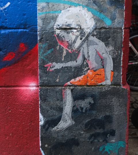 graffiti art, child wearing only orange shorts, seated, also wearing astronaut helmet, arm reaching out with fingers pointed