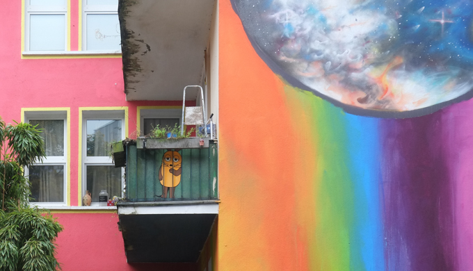 small yellow and brown painted animal on a balcony, beside a wall painted in rainbow colors with an image of the planet earth