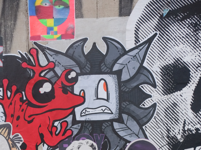 paste up graffiti pieces, A red frog clings to a character that looks rather concerned about that large skull lurking behind him.