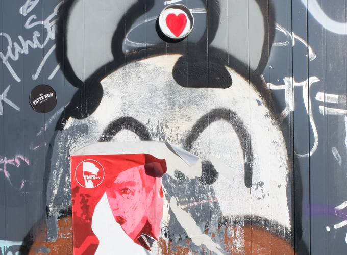 remains of face of cow, with red heart in jar lid above its head, and a torn red poster over one eye