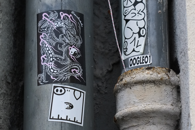 Three graffiti stickers on metal poles, all three are monochromatic black and white