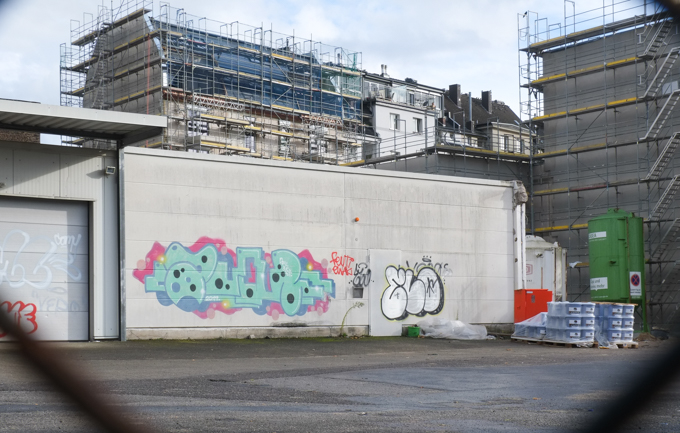 construction of new buildings behind a vacant lot, some graffiti tags on the wall