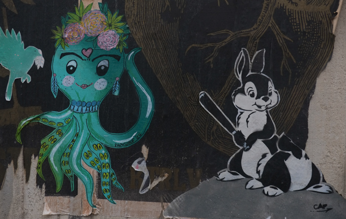 two paste ups, on the left an octopus and on the right, black and white rabbits with a baseball bat