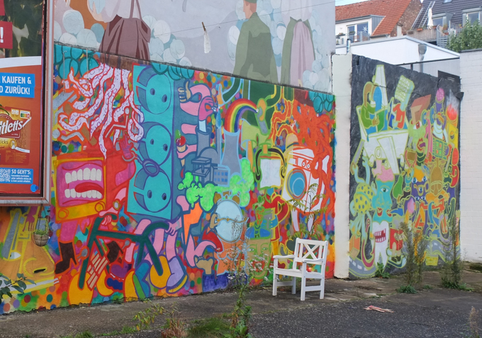 white chair sits in front of a colourful mural, street art, outdoors, 