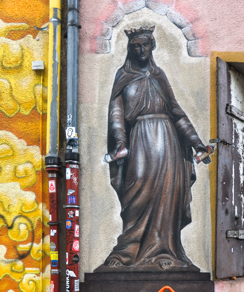 mural of a woman in medieval clothing, but with a can of spray paint in each hand
