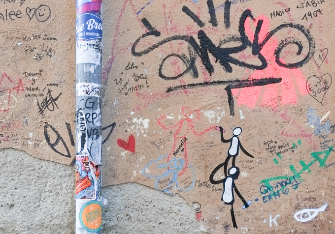 graffiti in Florence Italy by artist Exitenter, black drawing of two people, one standing on the shoulders of the other while drawing another red figure, lots of other written graffiti on the wall, mostly names and dates of people who had passed by