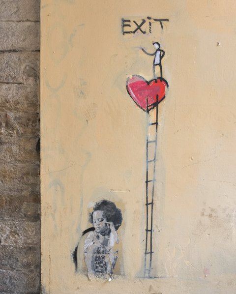 graffiti in Florence Italy by artist Exitenter, black drawing of a person standing on a large red heart that is at the top of a tall ladder.  at the bottom of the ladder is another graffiti, paste up, of a young girl sitting on the ground
