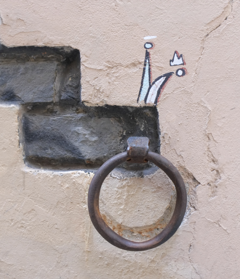 graffiti in Florence Italy by artist Exitenter, black drawing of a jester's hat (coloured in in white) and a little graffiti symbol crown, above a round door handle