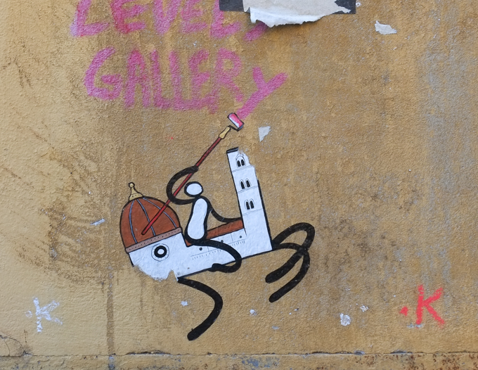 graffiti in Florence Italy by artist Exitenter, black drawing of a person holding a paint roller with pink paint, and riding on a horse that is really a Florence church