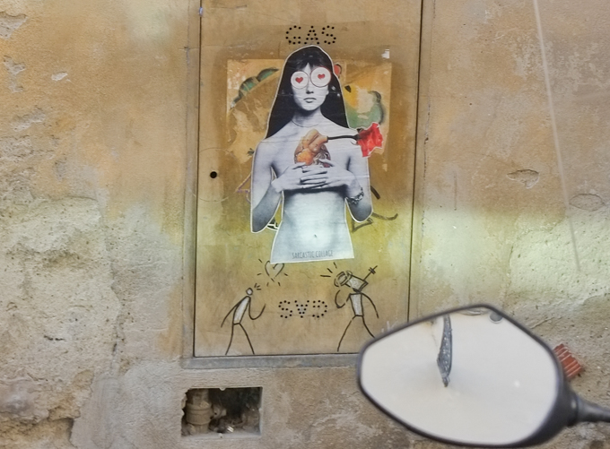 large paste up, wheatpaste, of a woman with hearts over her eyes, holding her anatomically correct heart that has a red rose coming out of it, below her are two little figures by exit enter, graffiti in Florence