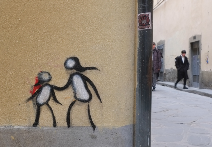two men walking on street, passing a building with 
graffiti in Florence Italy by artist Exitenter, black drawing of two people, one smaller than the other, like adult and child, 