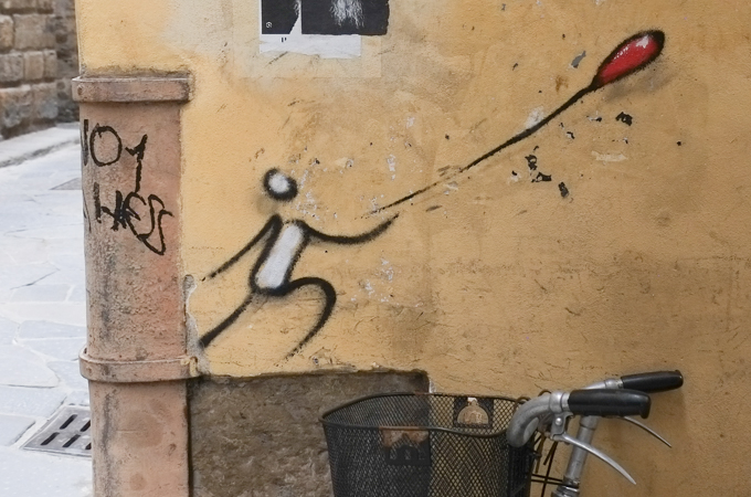 bike with black metal basket parked by an exit enter graffiti of a person trying to reach the string  attached to a red balloon that is being blown away