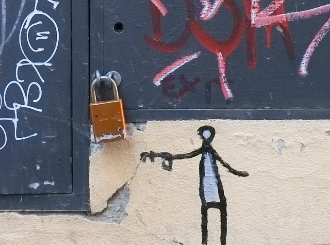 little drawing by artist exitenter of a little person holding a key, key is beside a real lock on a metal cabinet