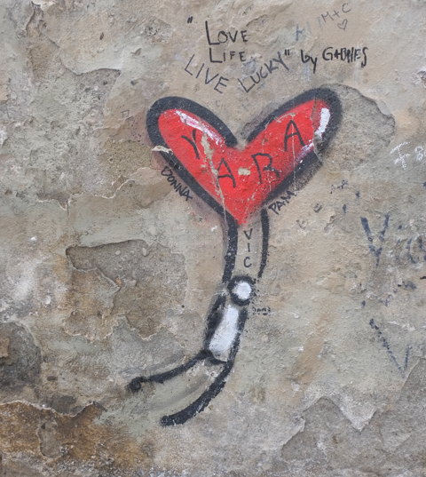 graffiti in Florence Italy by artist Exitenter, black drawing of a person holding onto a heart that has lifted him into the air, with lots of words written by other people, as graffiti, around it
