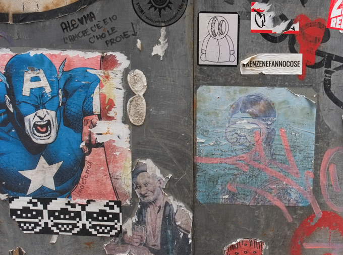 paste ups and graffiti on a door, a superhero in blue, an older man with a glass in his hand, a piece by blub of a woman with goggles on, 