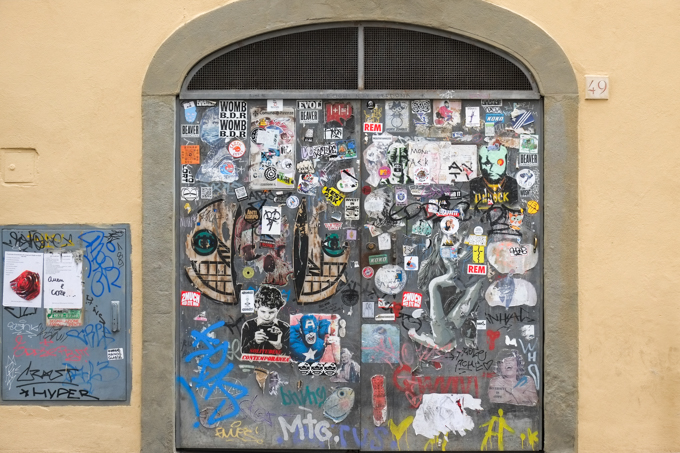 A double grey door with rounded arch, lots of graffiti, paste ups and stickers on it, 
