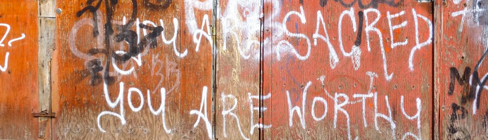 part of a garage door with scribbles graffiti, also words that say you are sacred, you are worthy