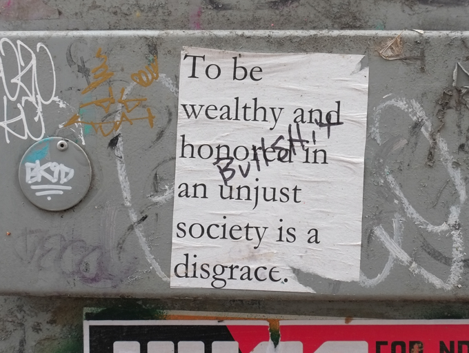 sticker that says to be wealthy and honored in an unjust society is a disgrace.  someone has written bullshit across it. 
