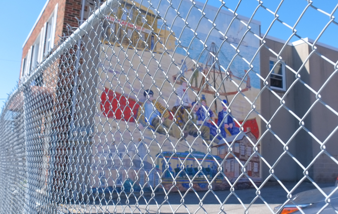 behind a fence, people sitting on the beach, Barnharts dance pavillion, in a mural by Tony Johnson