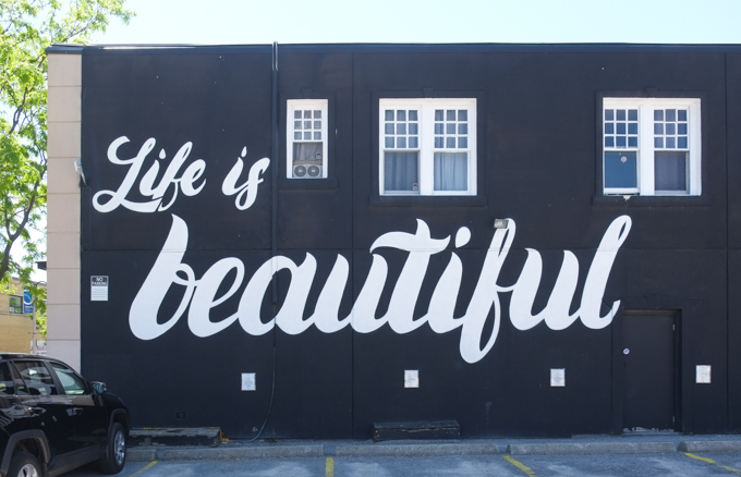 Side of building painted black, with street art calligraphy in cursive, life is beautiful