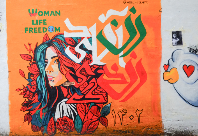 orange poster with words, woman, life freedom.  also some Arabic letters, image of a woman with long dark hair, in profile