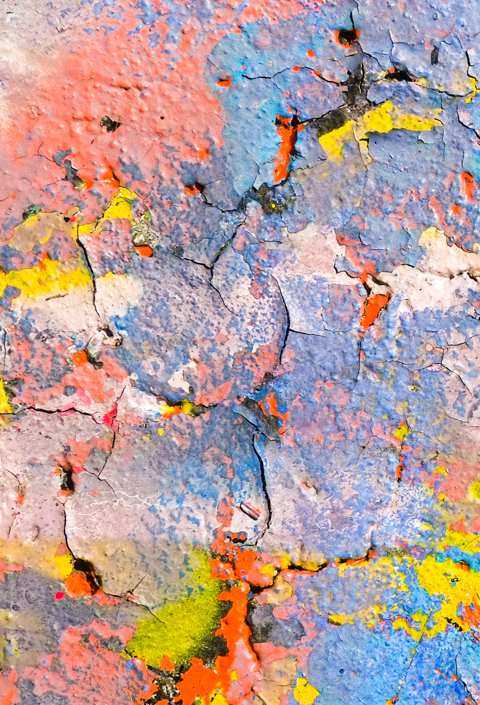 cracks in the layers of paint on a wall, many shade of blue and red, with some yellow