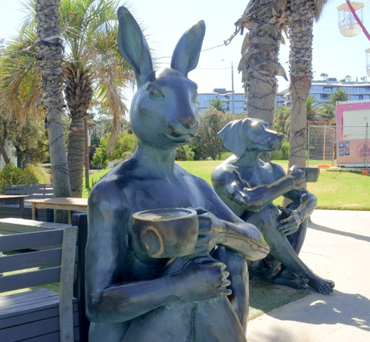 sculptures, rabbitwoman and dogman, sitting outsidde cafe on st. kilda beach, having a drink, creation of artists Gillie and Marc