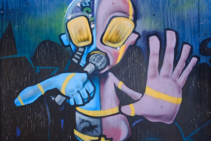 part of a larger mural by Eastthree in Honolulu, creature singing or speaking into a microphone held close to its mouth, with one hand up in a 'stop' gesture