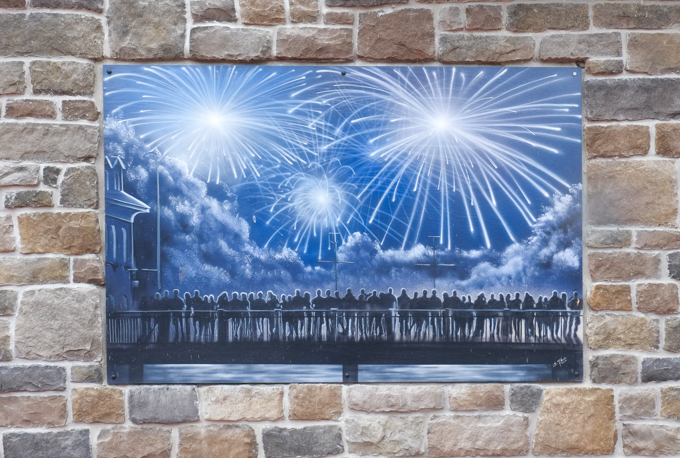 silhouette of many people standing on a bridge watching a fireworks display, picture mounted on stone wall