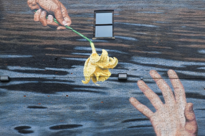 street art mural in Lynn Massachusetts by B K Foxx, two hands interacting over water, one hand is giving a daffodil to the other which happens to be in the water