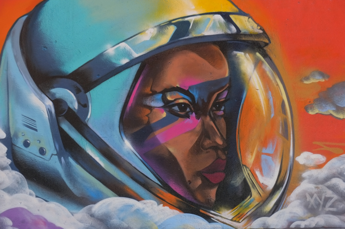 street art mural on wall of railway underpass on Bloor street West, by Danilo Deluxo, a woman in an elaborate helmet, futuristic pilot.