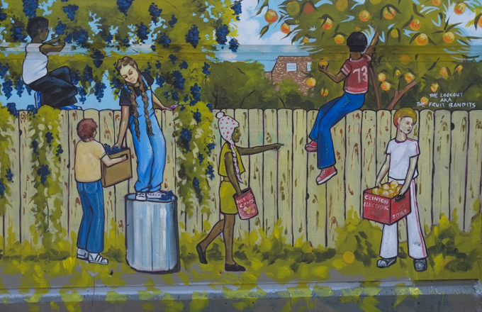 street art mural on wall of railway underpass on Bloor street West, by Jim Bravo, a group of children is picking fruit from trees that are on the other side of a fence, title is fruit bandits