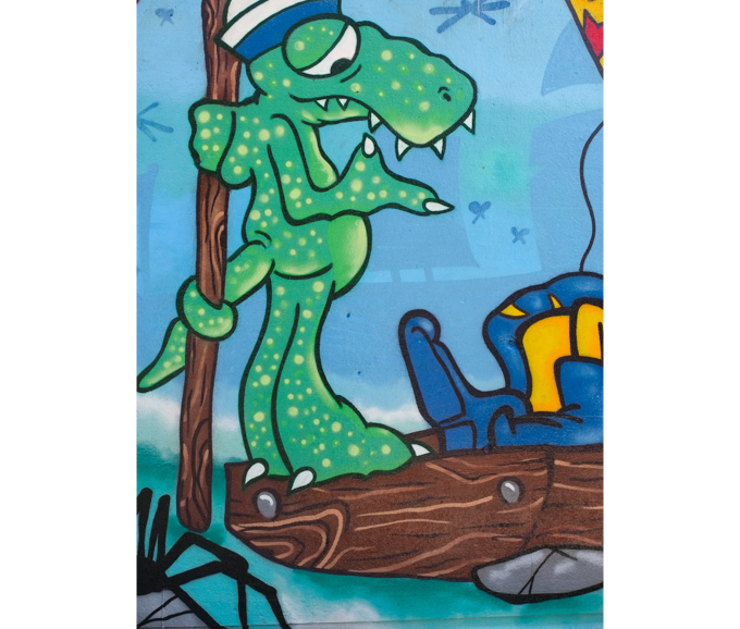 street art mural on wall of railway underpass on Bloor street West by Getso, a green crocdile, standing, with tail wrapped around a brown pole, beside water