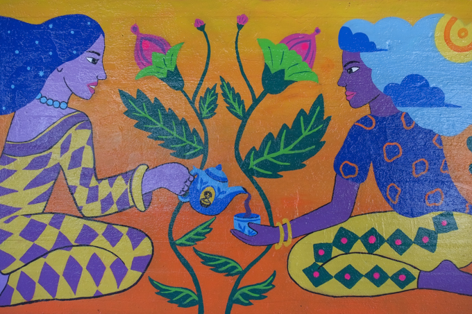 street art mural on wall of railway underpass on Bloor street West by Ghazaraza, two ladies are sharing a pot of tea, seated on the ground facing each other.  Pink flowers in the middle