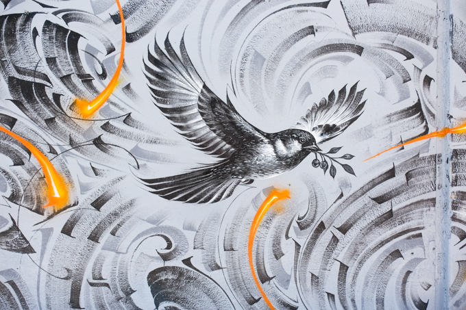 street art mural on wall of railway underpass on Bloor street West A peace dove with an olive branch in its beak, in a swirl of calligraphy, by Medeio, monotone grey
