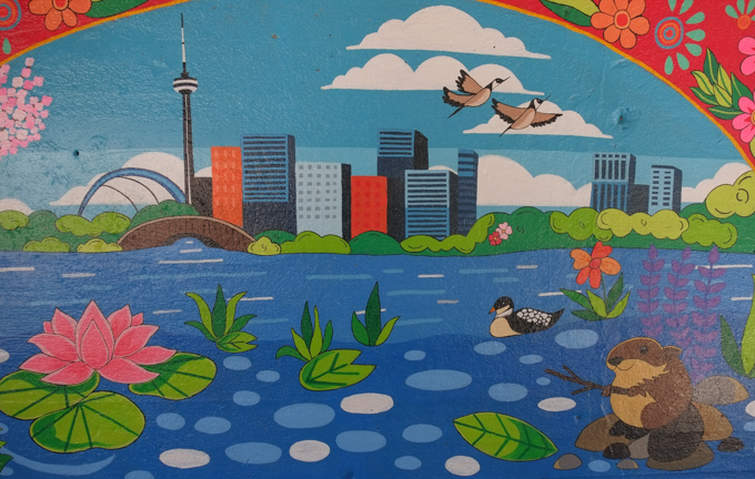 street art mural on wall of railway underpass on Bloor street West painte by Opola Karim, showing Toronto Harbour and Toronto skyline in a very stylized design, loon in water, beaver on a rock, Canada geese flying overhead 