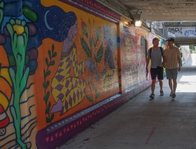 two men walking past street art murals on the wall of railway underpass on Bloor street West