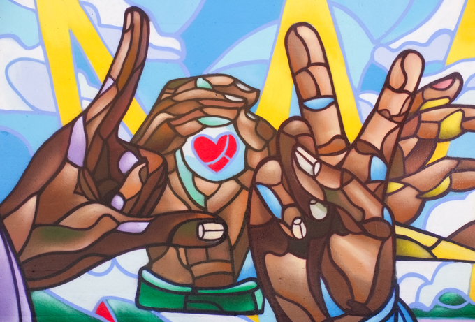 street art mural on wall of railway underpass on Bloor street West, by Phillip Saunders, a k a Love is here.  Four hands in shades of beige and brown, 2 with peace sign, one holding a round object with a red heart on it, 