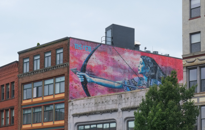 street art mural in Lynn Massachusetts, woman archer, warrior, with bow and arrow raised, on red background