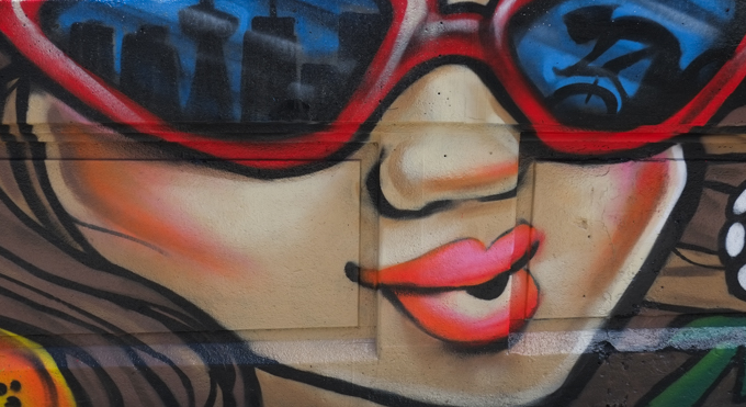 street art mural on wall of railway underpass on Bloor street West by EGR, woman with sunglasses that reflected Toronto skyline and a person cycling past, red rims and blue glass