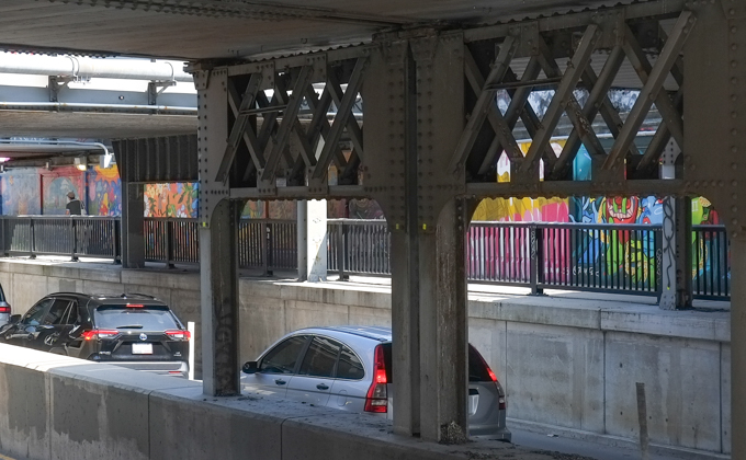 street art mural on wall of railway underpass on Bloor street West as seen from across the street metal girders supporting bridge, traffic on the road, 