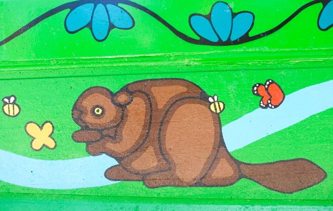 street art mural on wall of railway underpass on Bloor street West, by Waskwane Designs, animal, beaver beside a river