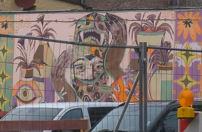 urban art, street art, in Cologne Germany, near Ehrenfeld station, Potted plants, and/or plants in colourful vases surround a person who seems to be removing an animal (leopard?) mask in a mural painted by Gaupo Sapo