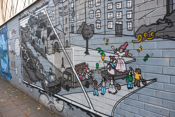 Belgian Quarter mural, war time city scene in greys, with after war peacetime in bright colours