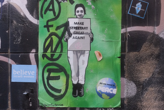 urban art, street art, in Cologne Germany, near Ehrenfeld station, green poster with image of woman holding a sign that says make street art great again, also a small sticker says believe israeli women as well as small round sticker saying all we need is peace