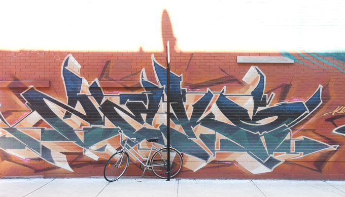 bike parked against street sign pole in front of a wild style text graffiti painting