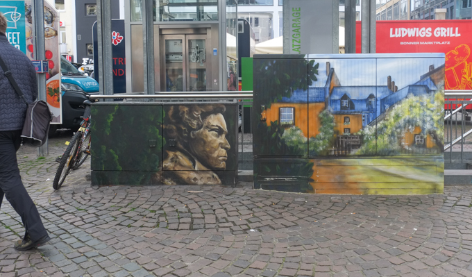 two sidewalk utility boxes,side by side, in Bonn Germany,painted with portrait of JS Bach and with a picture of an old house