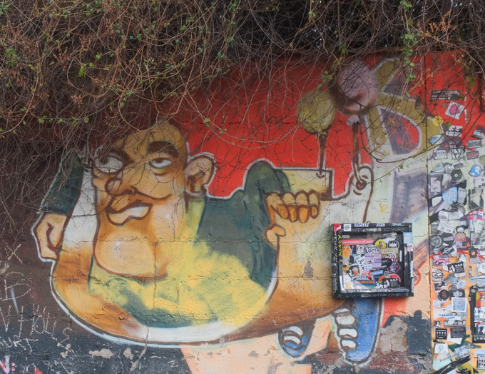urban art, street art, in Cologne Germany, near Ehrenfeld station, older painting of a man on a wall where plants have grown over the top of the wall and look like his hair