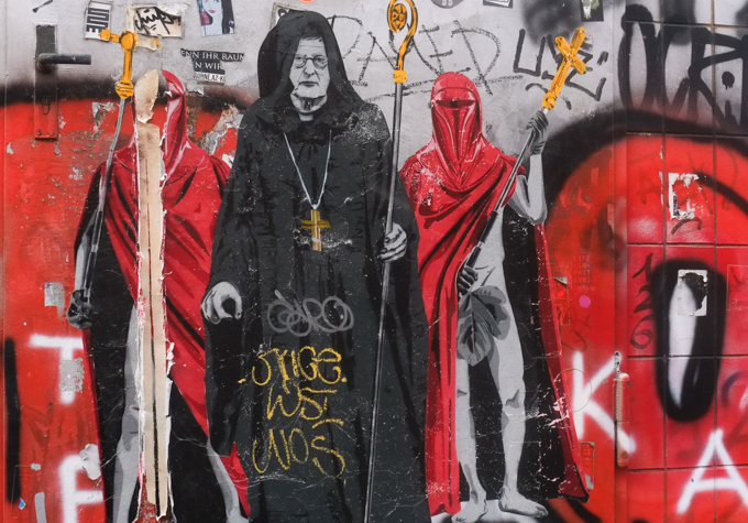 urban art, street art, in Cologne Germany, near Ehrenfeld station, SeiLeise stencil, archbishop in black hooded robe, holding staff, accompanied by men draped in red so heads are hidden but fig leaf over groin