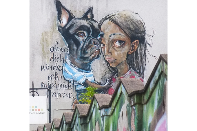 by Herakut, a girl and her dog. dog is wearing blue and white striped t shirt. text on mural says Ohne dich würde ich mich nicht trauen